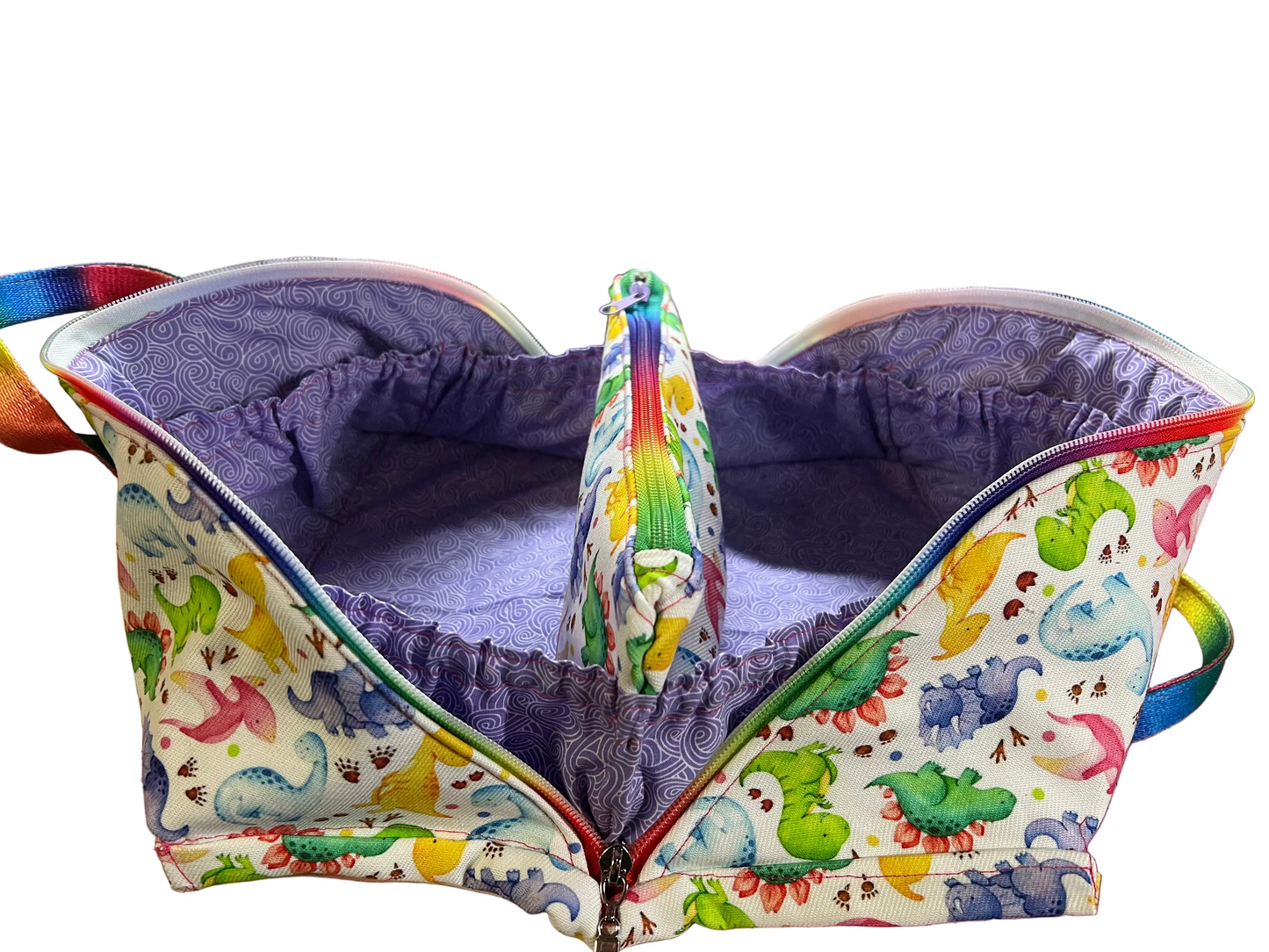 A  fabric organizer pouch with a colorful dinosaur print on the exterior and a purple patterned lining, shown open on a sewing table.