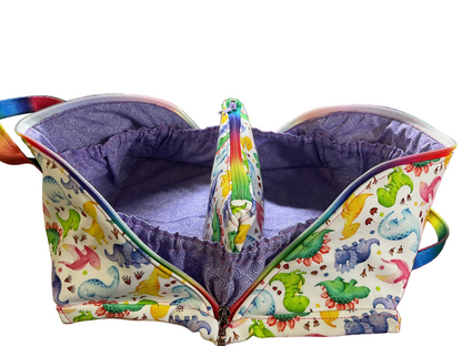 A  fabric organizer pouch with a colorful dinosaur print on the exterior and a purple patterned lining, shown open on a sewing table.